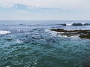Calm ocean waves meet rock formations under a clear sky.