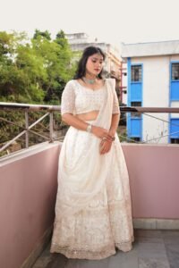 Woman wearing traditional Indian lehenga on a balcony with urban backdrop.