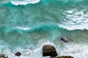 Stunning aerial view of turquoise ocean waves crashing on a rocky shoreline, ideal for travel and nature themes.