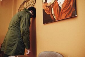 A man leaning his head against a wall, facing an abstract painting in a contemplative mood.